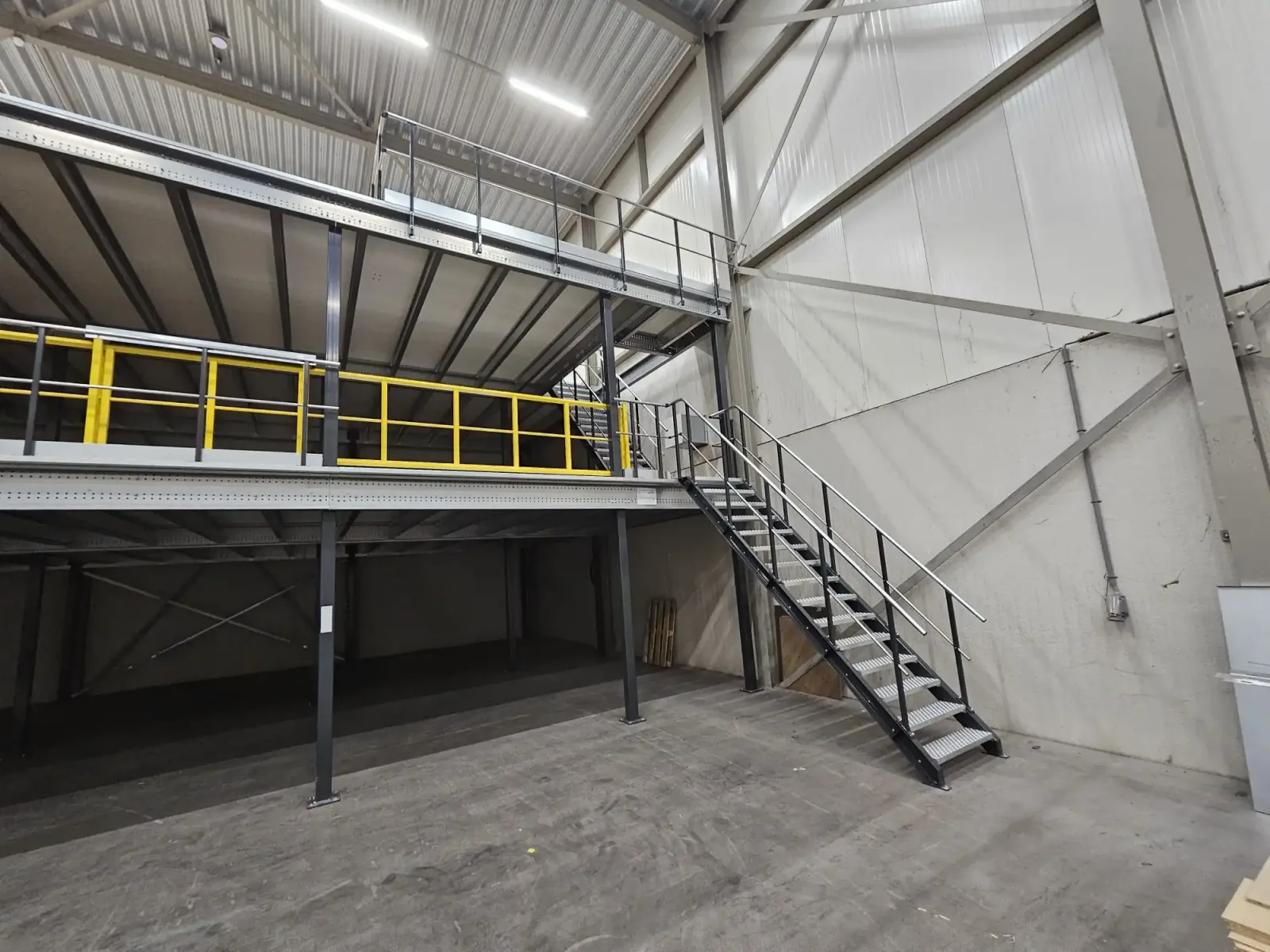 Altivo steel mezzanine floor in a warehouse, with access stairs and a yellow pallet gate