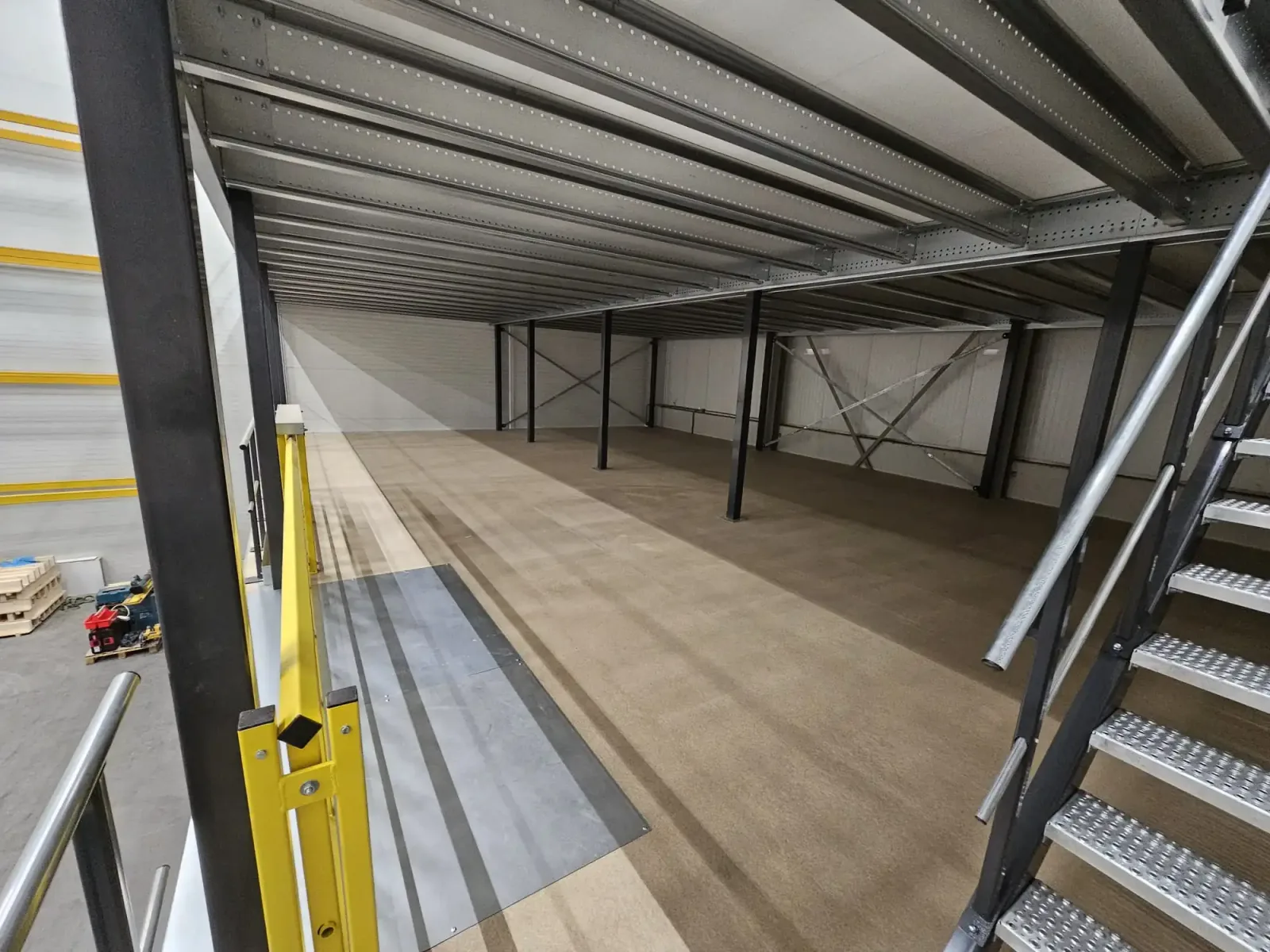 Steel mezzanine structure from below, showing beams, columns and the access stairs