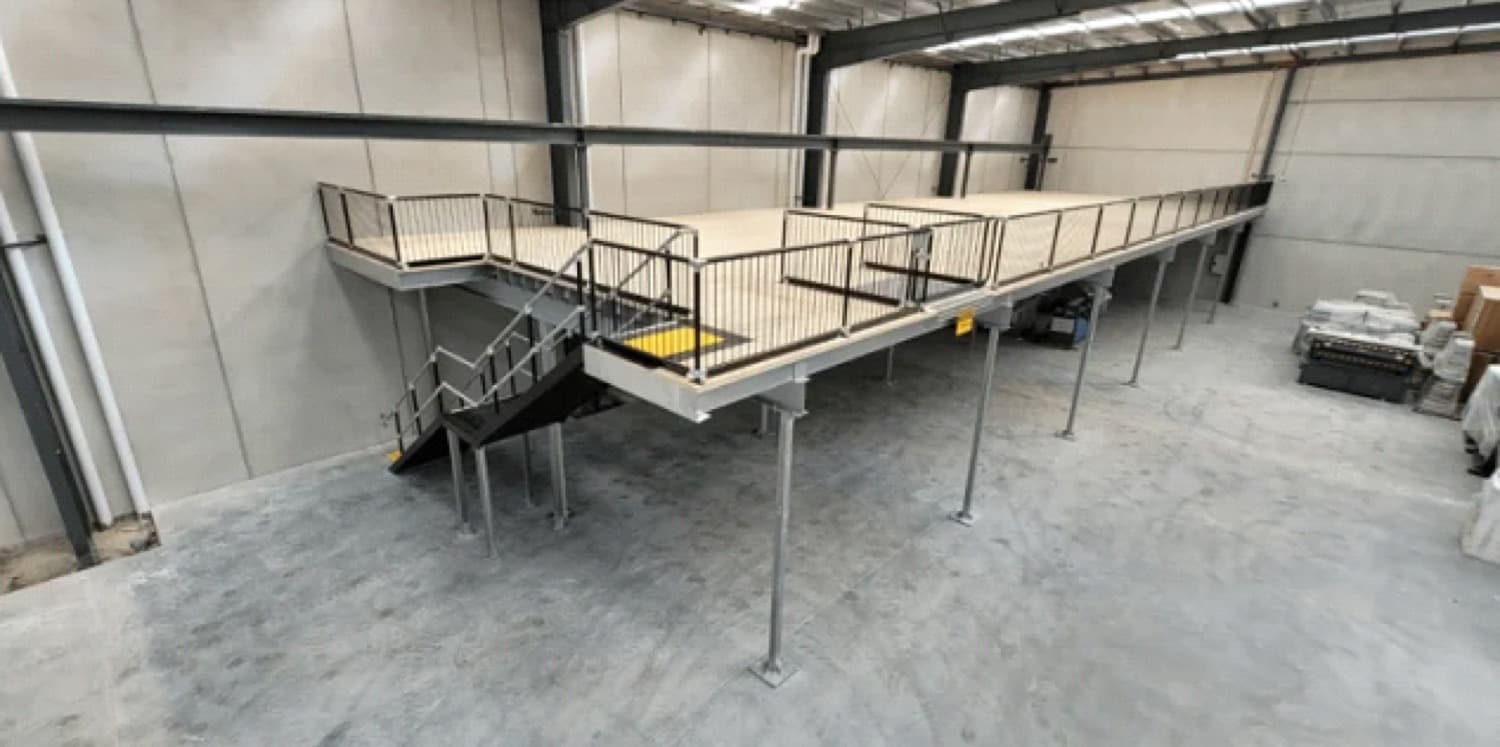 Pallets stored on a steel mezzanine floor behind a rollover pallet gate